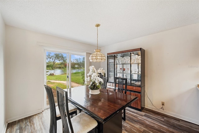 dining space featuring a textured ceiling, a water view, and dark hardwood / wood-style floors