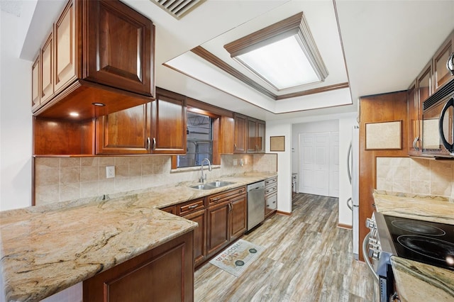 kitchen with light wood-type flooring, light stone counters, stainless steel appliances, a raised ceiling, and sink