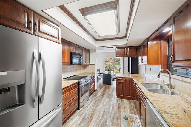 kitchen with hanging light fixtures, sink, light hardwood / wood-style flooring, decorative backsplash, and appliances with stainless steel finishes