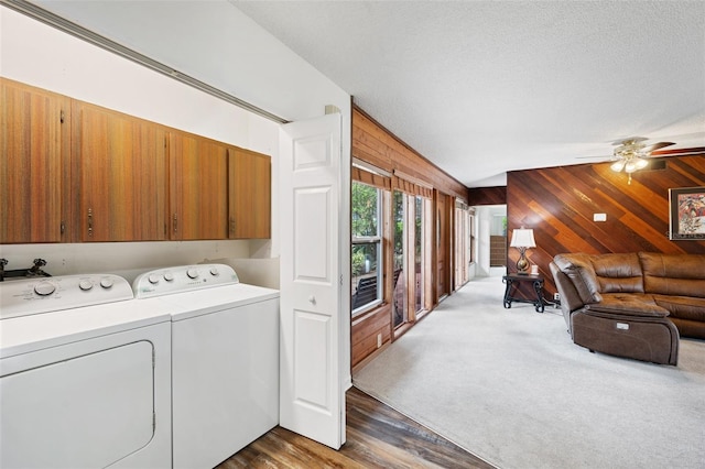 clothes washing area with cabinets, a textured ceiling, washer and dryer, dark hardwood / wood-style floors, and wood walls