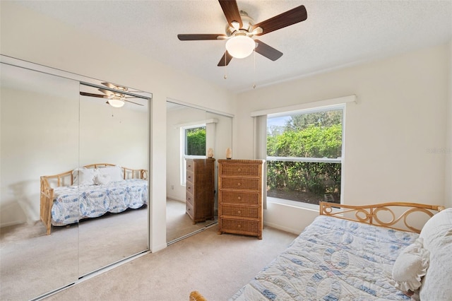 carpeted bedroom with a textured ceiling, multiple windows, multiple closets, and ceiling fan