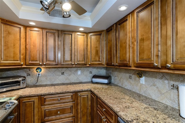 632 Edgewater Dr Unit 532, Dunedin, FL 34698 - kitchen featuring ceiling fan, a raised ceiling, tasteful backsplash, brown cabinetry, and light stone counters