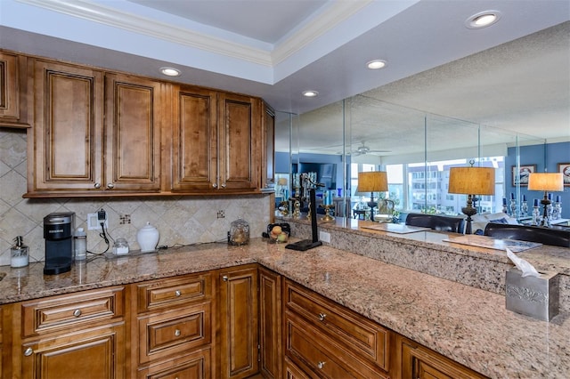 kitchen featuring ceiling fan, tasteful backsplash, light stone counters, crown molding, and decorative light fixtures