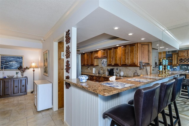632 Edgewater Dr Unit 532, Dunedin, FL 34698 - kitchen with crown molding, decorative backsplash, a sink, light stone countertops, and a kitchen breakfast bar