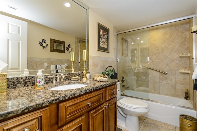 full bathroom featuring vanity, shower / bath combination with glass door, tile walls, tile patterned flooring, and toilet