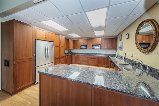 kitchen with light wood-type flooring, kitchen peninsula, stainless steel appliances, and dark stone counters