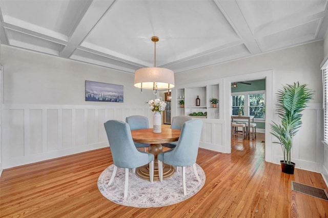 dining area featuring beamed ceiling, coffered ceiling, built in shelves, and light hardwood / wood-style floors