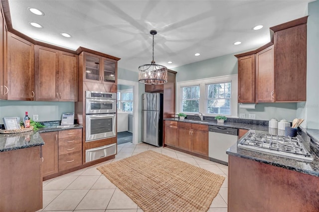 kitchen featuring hanging light fixtures, light tile patterned floors, appliances with stainless steel finishes, a notable chandelier, and dark stone counters