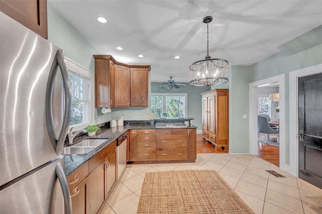 kitchen with sink, hanging light fixtures, stainless steel appliances, light tile patterned flooring, and ceiling fan with notable chandelier