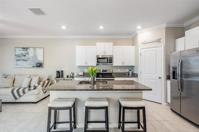 kitchen with appliances with stainless steel finishes, ornamental molding, a center island with sink, white cabinets, and a breakfast bar area