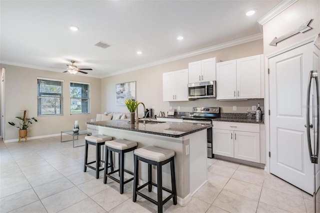 kitchen with sink, an island with sink, dark stone counters, white cabinets, and appliances with stainless steel finishes