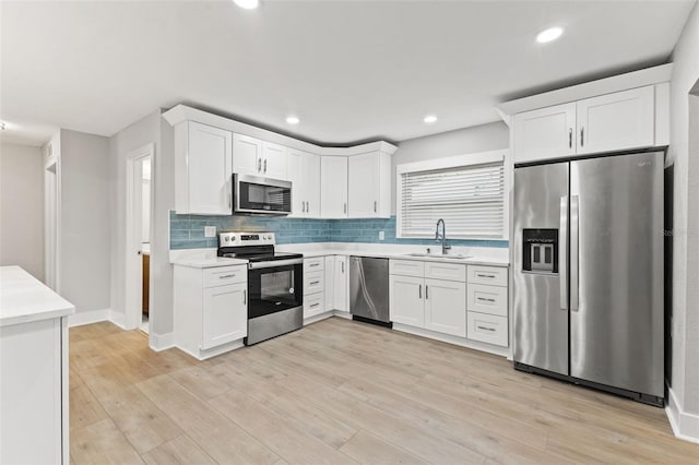 kitchen with appliances with stainless steel finishes, light wood-type flooring, white cabinetry, and sink