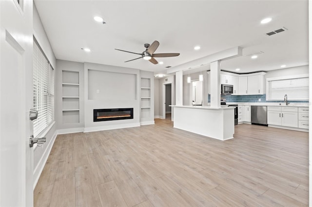 unfurnished living room featuring built in features, light hardwood / wood-style flooring, a healthy amount of sunlight, and sink