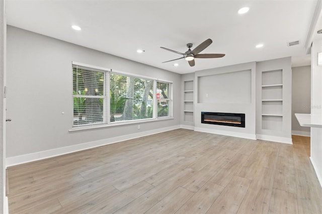 unfurnished living room with built in shelves, light hardwood / wood-style flooring, and ceiling fan