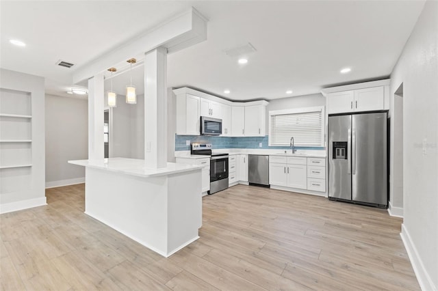 kitchen featuring white cabinets, appliances with stainless steel finishes, light wood-type flooring, and pendant lighting