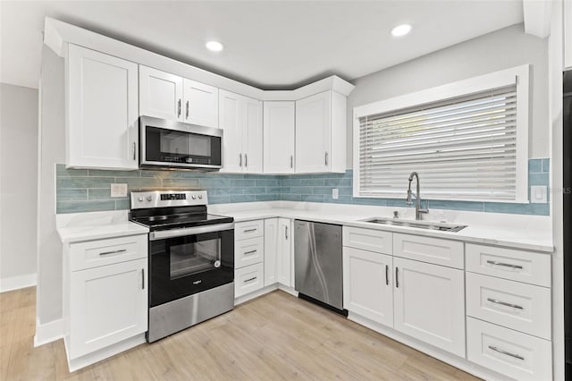 kitchen featuring white cabinets, sink, decorative backsplash, light wood-type flooring, and appliances with stainless steel finishes