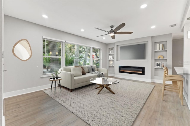 living room featuring ceiling fan, built in features, and light wood-type flooring