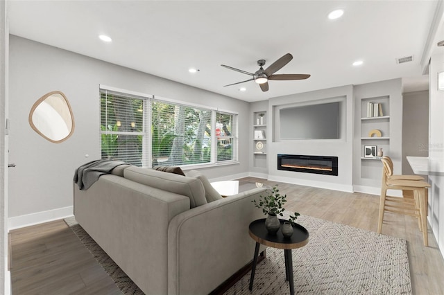 living room with built in features, hardwood / wood-style flooring, and ceiling fan