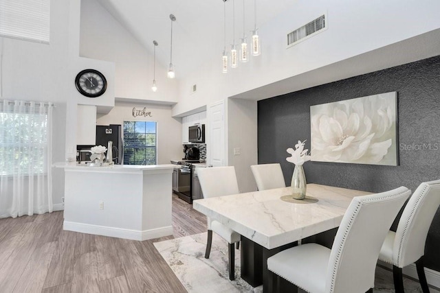 dining room with light hardwood / wood-style flooring and high vaulted ceiling