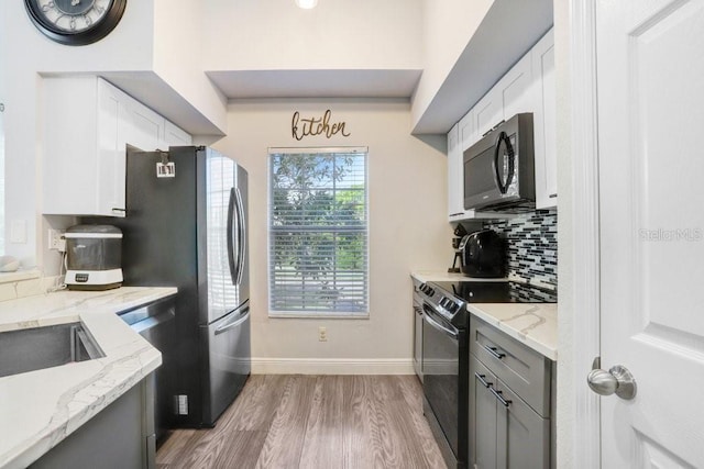 kitchen featuring light stone countertops, white cabinetry, stainless steel appliances, and light wood-type flooring