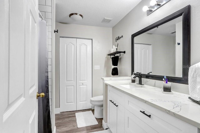 bathroom with hardwood / wood-style floors, vanity, toilet, and a textured ceiling