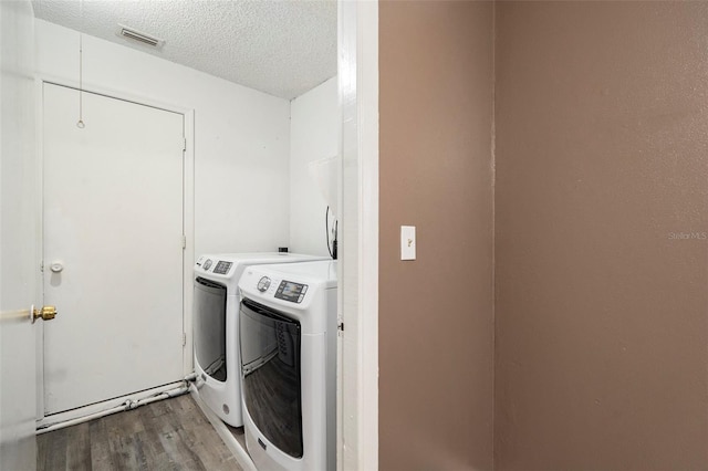 clothes washing area with washer and dryer, a textured ceiling, and hardwood / wood-style flooring