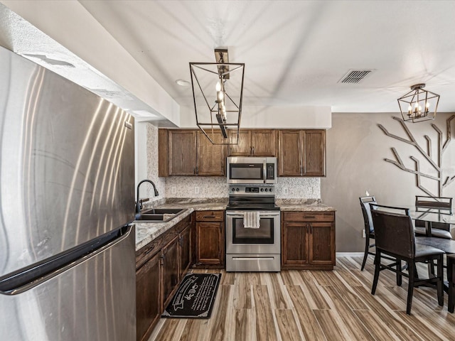 kitchen with decorative light fixtures, sink, appliances with stainless steel finishes, and light hardwood / wood-style flooring