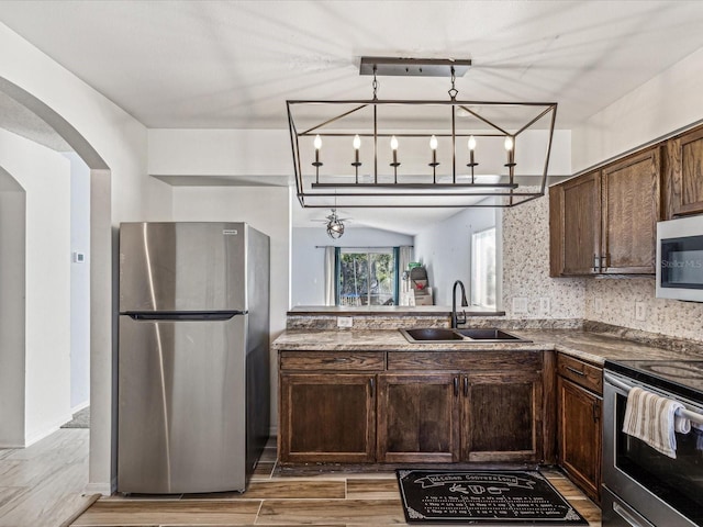 kitchen featuring sink, light hardwood / wood-style flooring, appliances with stainless steel finishes, a notable chandelier, and dark brown cabinetry