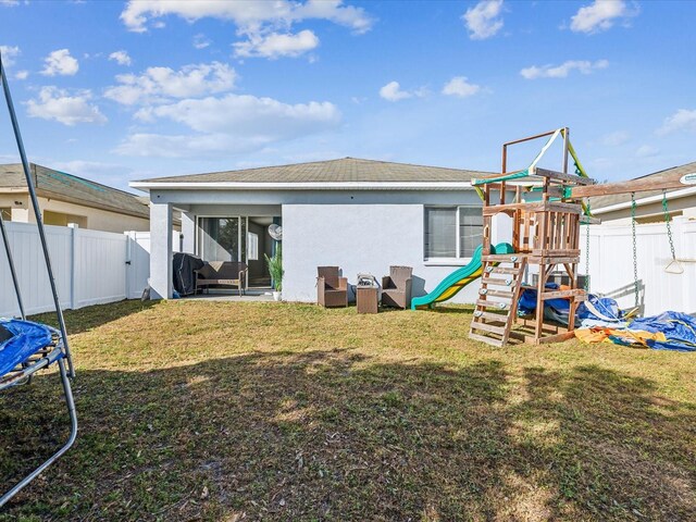 rear view of house featuring a playground, a trampoline, and a yard