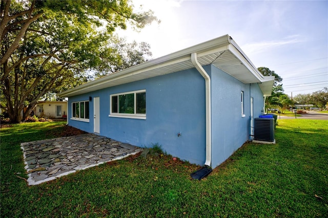 1042 Idlewild Dr N, Dunedin, FL 34698 - view of side of home featuring central AC unit, stucco siding, a lawn, and a patio area
