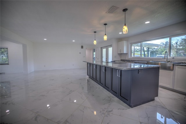 kitchen featuring light stone countertops, decorative light fixtures, white cabinetry, and sink