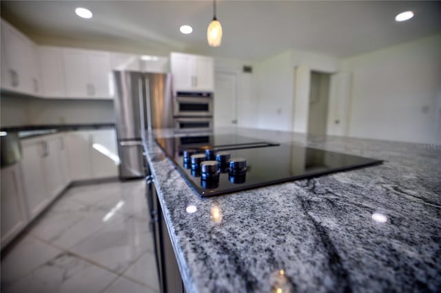 kitchen with pendant lighting, black electric stovetop, dark stone countertops, stainless steel double oven, and white cabinetry