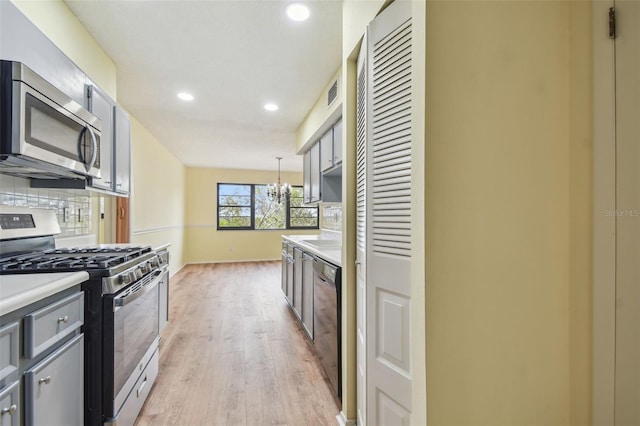 kitchen featuring appliances with stainless steel finishes, backsplash, pendant lighting, an inviting chandelier, and light hardwood / wood-style flooring