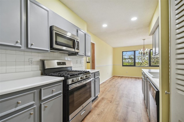 kitchen with gray cabinetry, hanging light fixtures, stainless steel appliances, an inviting chandelier, and light wood-type flooring