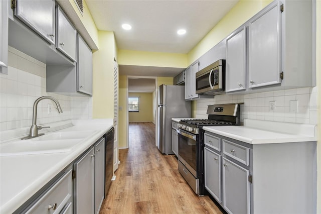 kitchen with backsplash, gray cabinets, light wood-type flooring, and appliances with stainless steel finishes