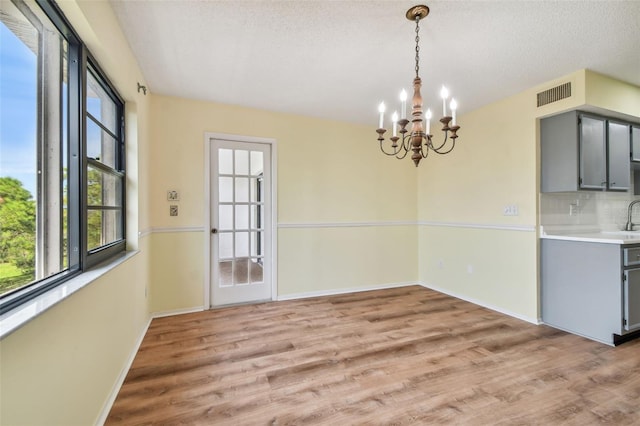 unfurnished dining area featuring light wood-type flooring, a textured ceiling, and a notable chandelier