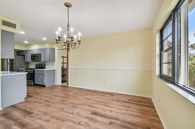 kitchen featuring gray cabinets, plenty of natural light, an inviting chandelier, and appliances with stainless steel finishes