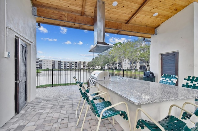 view of patio with area for grilling, a water view, an outdoor bar, and an outdoor kitchen