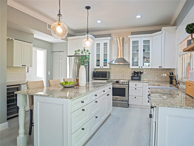 kitchen featuring stainless steel appliances, wall chimney range hood, decorative light fixtures, white cabinets, and wine cooler