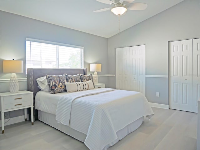 bedroom with light wood-type flooring, vaulted ceiling, ceiling fan, and multiple closets