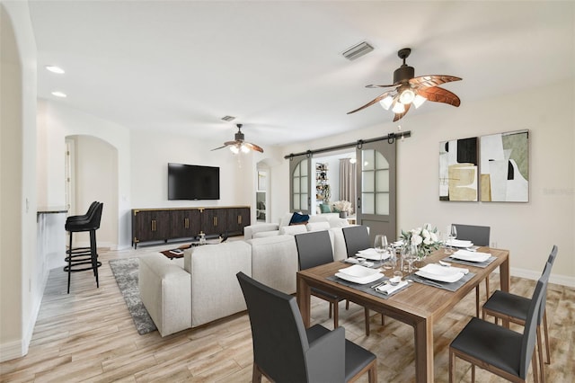 dining area featuring a barn door, light hardwood / wood-style floors, and ceiling fan