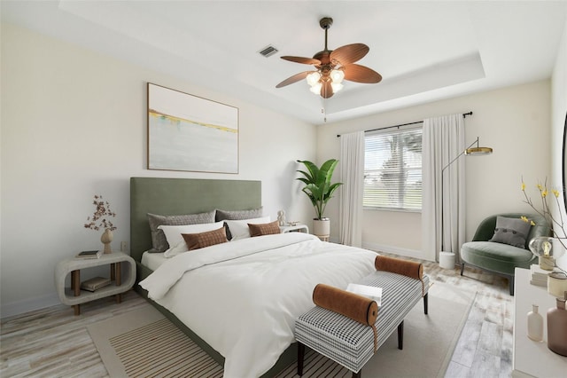 bedroom with a tray ceiling, ceiling fan, and light wood-type flooring