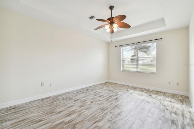 unfurnished room featuring light hardwood / wood-style floors, ceiling fan, and a tray ceiling