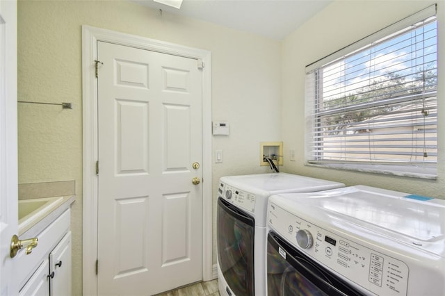 clothes washing area with washer and clothes dryer, light hardwood / wood-style floors, cabinets, and sink