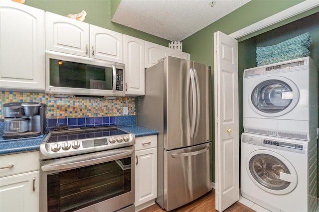 kitchen with appliances with stainless steel finishes, stacked washer and dryer, white cabinetry, and tasteful backsplash