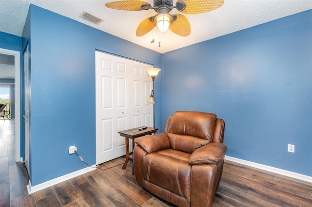 living area with ceiling fan, dark wood-type flooring, and a textured ceiling