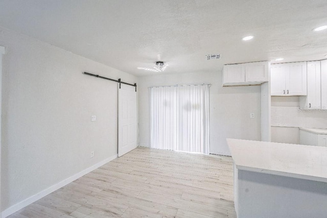 kitchen featuring decorative backsplash, white cabinetry, a barn door, and light wood-type flooring