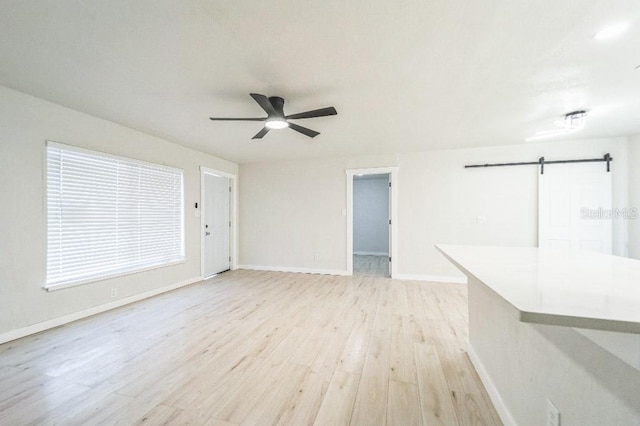 unfurnished living room with ceiling fan, a barn door, and light hardwood / wood-style flooring