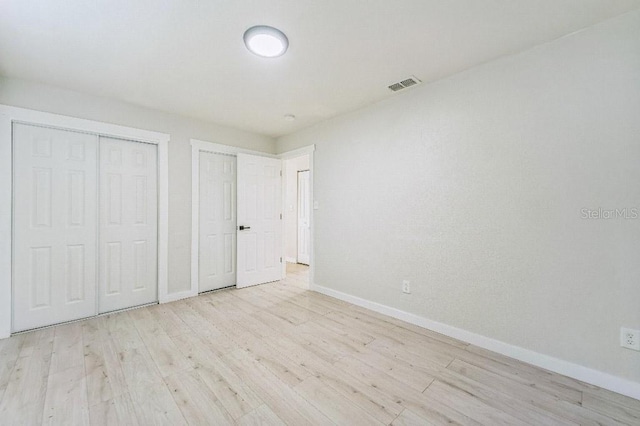 unfurnished bedroom with two closets and light wood-type flooring