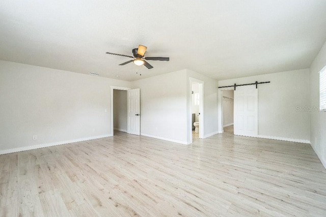 spare room featuring ceiling fan, a barn door, and light hardwood / wood-style floors